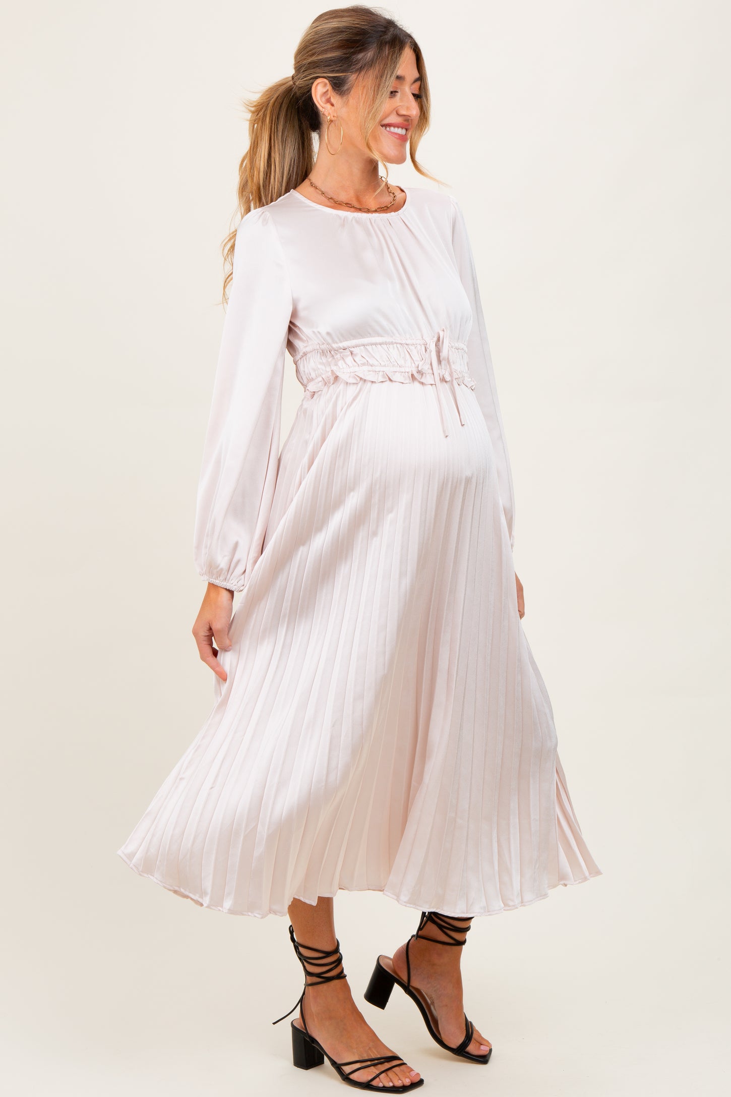 woman wearing a light pink maternity dress with a cinched waist and long sleeves, showcasing her baby bump