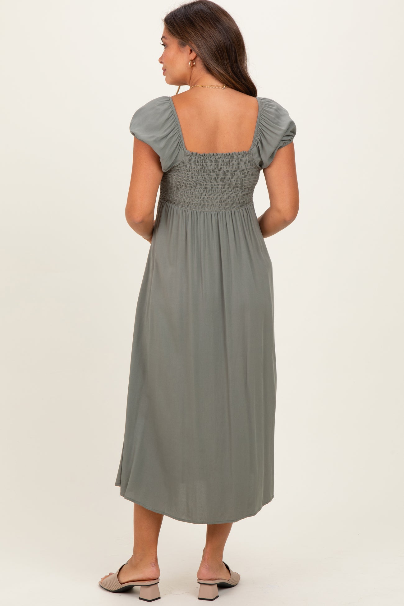 woman wearing a sage green maternity dress with puff sleeves and a smocked back, viewed from the back