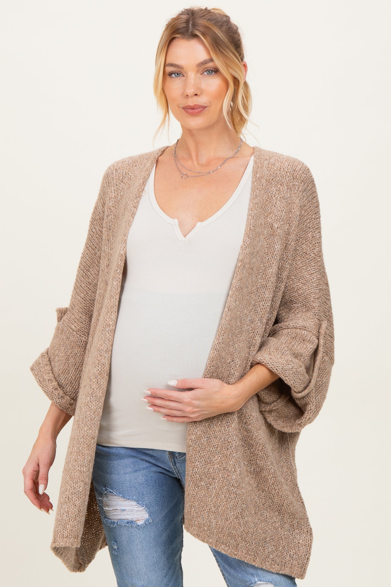 woman wearing a beige open-front cardigan over a white v-neck top and holding her baby bump, maternity wear