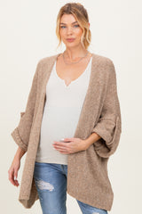 woman wearing a beige open-front cardigan over a white v-neck top and holding her baby bump, maternity wear