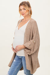 woman wearing a beige maternity cardigan over a white top and holding her baby bump with distressed jeans