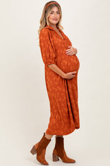 woman wearing an orange maternity dress with a leaf pattern, holding her baby bump and standing in a side pose