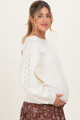 woman wearing a cream maternity sweater with lace detail, cradling her baby bump