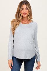 woman wearing a gray long sleeve maternity top with a visible baby bump and blue jeans