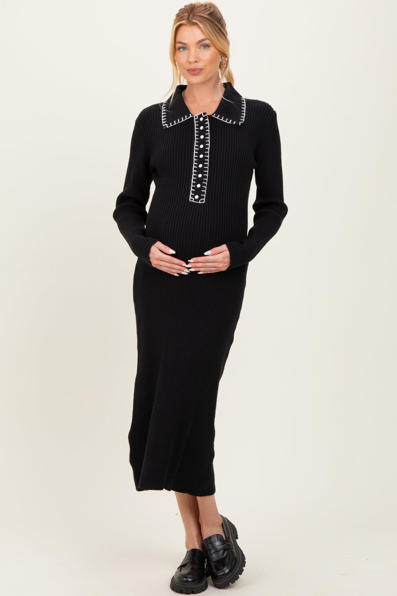 woman wearing a black ribbed maternity dress with a collar and button details, holding her baby bump
