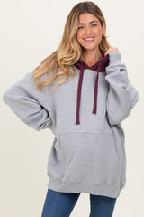 woman wearing a gray maternity hoodie with a maroon hood and pockets styled with blue jeans
