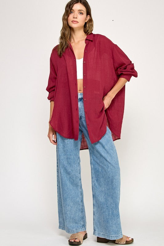 woman wearing a burgundy oversized button-up shirt, white crop top, and light blue wide-leg jeans
