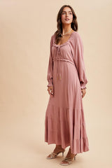 woman wearing a dusty rose long sleeve maxi dress with a drawstring neckline and tiered skirt