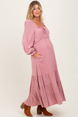 woman wearing a pink maternity maxi dress with puff sleeves and tiered skirt, showing her baby bump and standing in profile