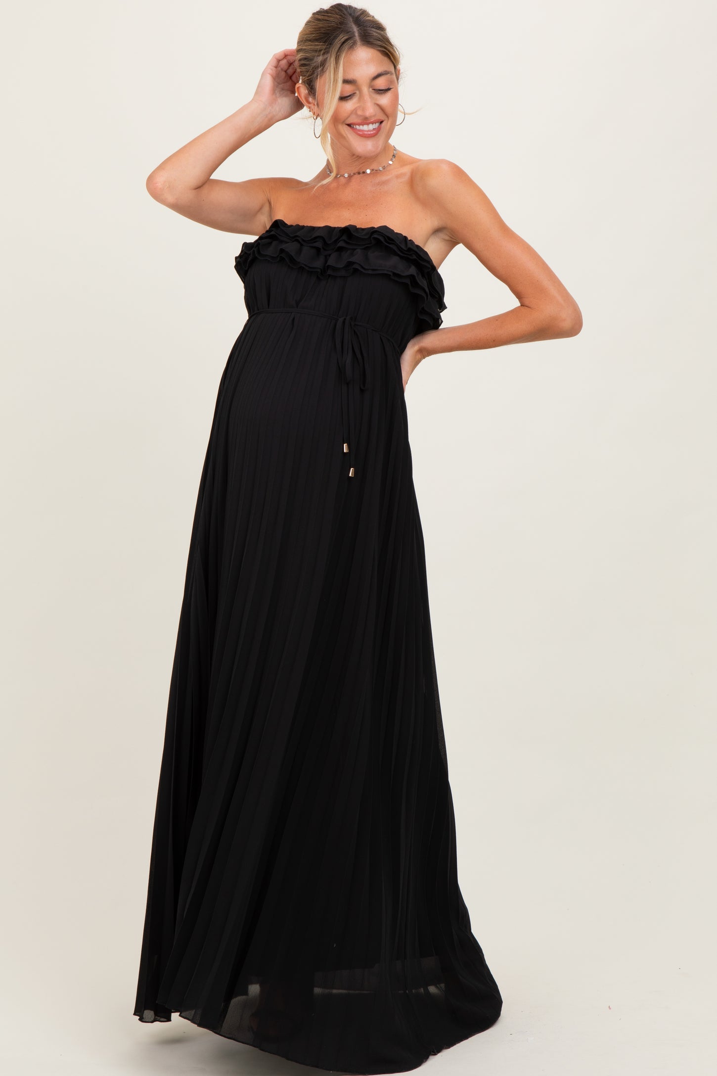 woman wearing a black strapless pleated maternity dress with ruffle detailing and a visible baby bump