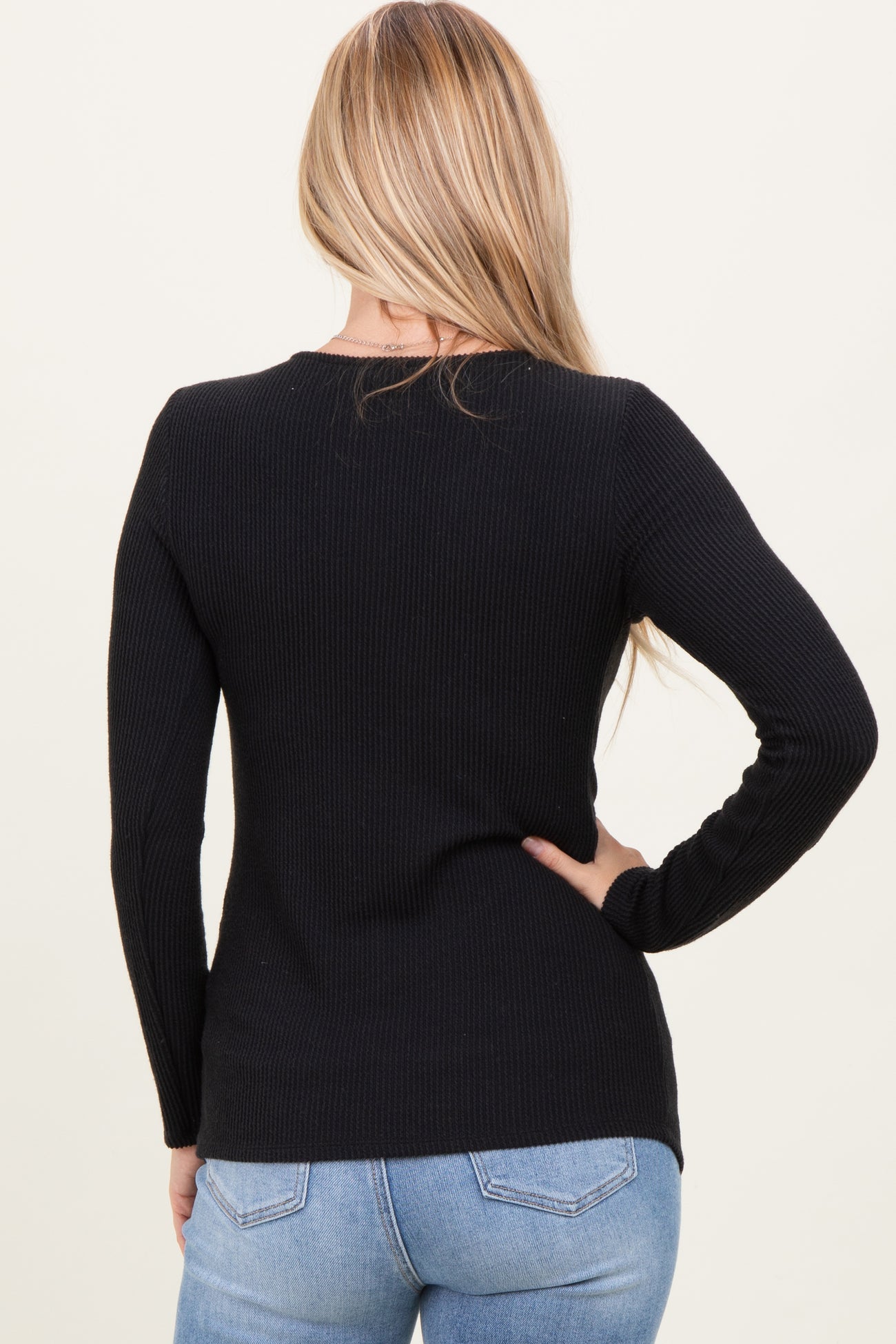 woman wearing a black ribbed long sleeve sweater with a fitted silhouette, shown from the back