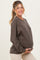 woman wearing a brown maternity sweatshirt and holding her baby bump, smiling at the camera