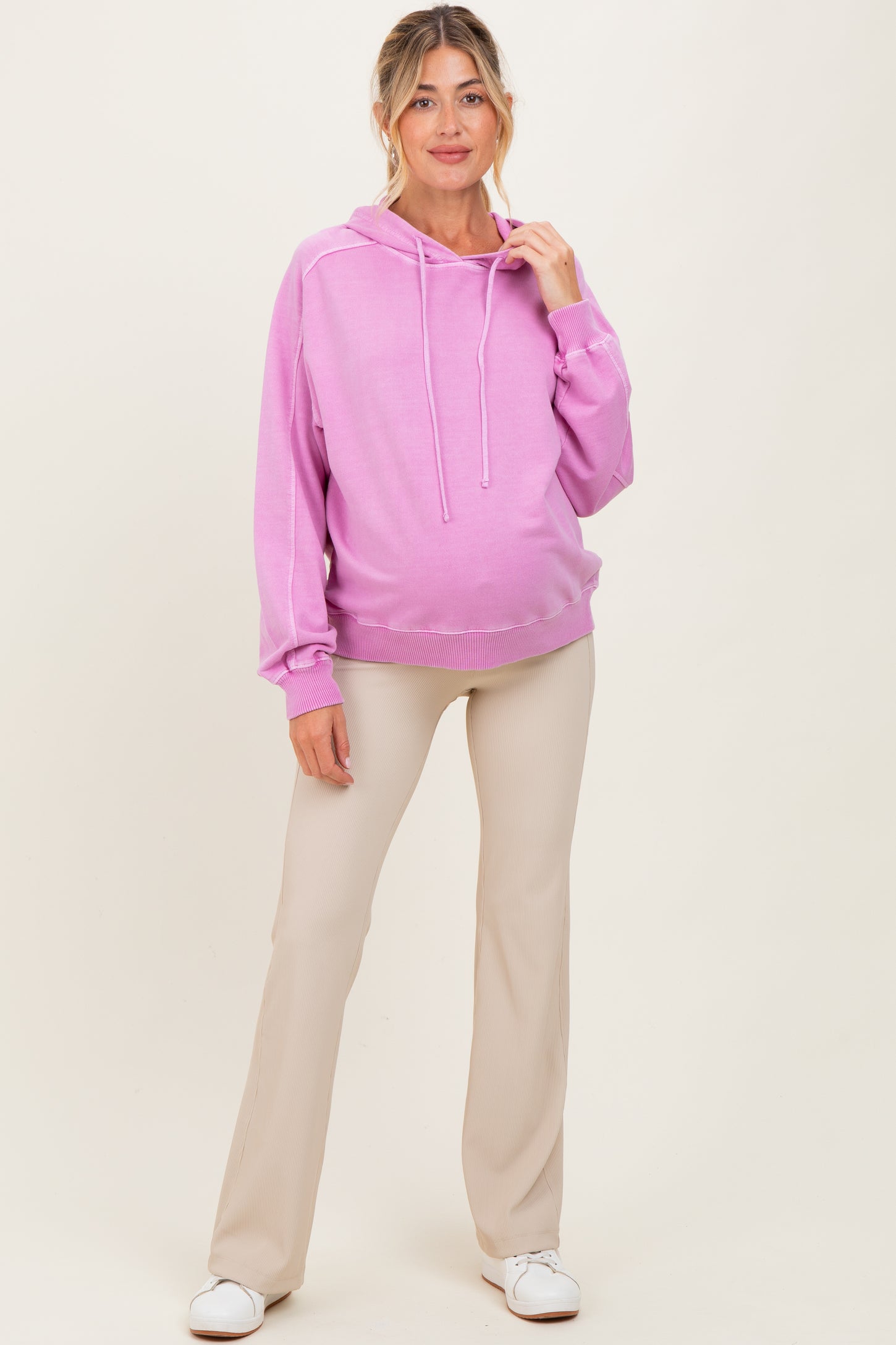 woman wearing a light pink maternity hoodie and beige pants, showing her baby bump