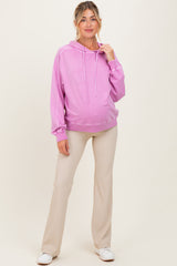 woman wearing a light pink maternity hoodie and beige pants, showing her baby bump