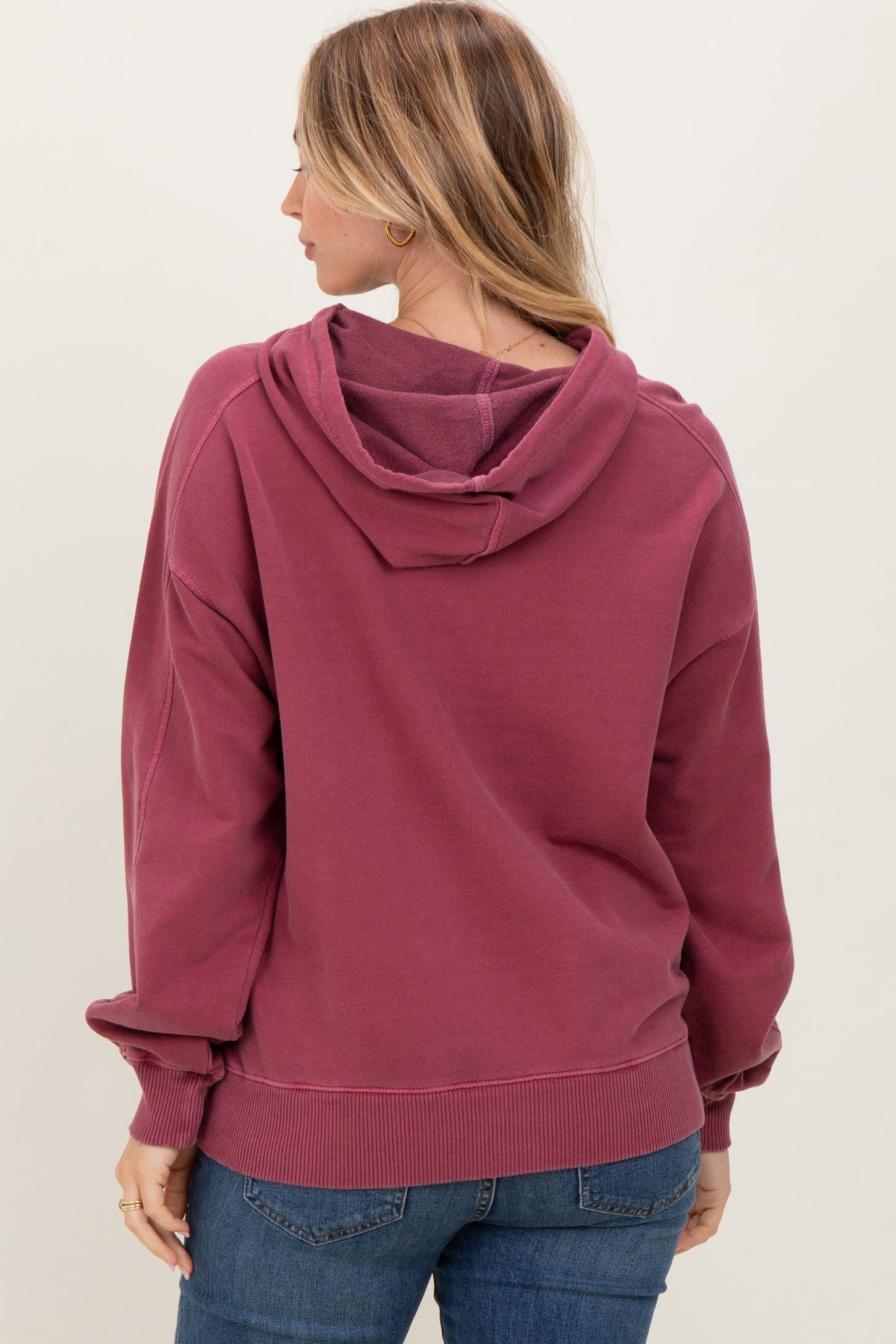 woman wearing a maroon oversized hoodie with a hood and ribbed cuffs, viewed from the back