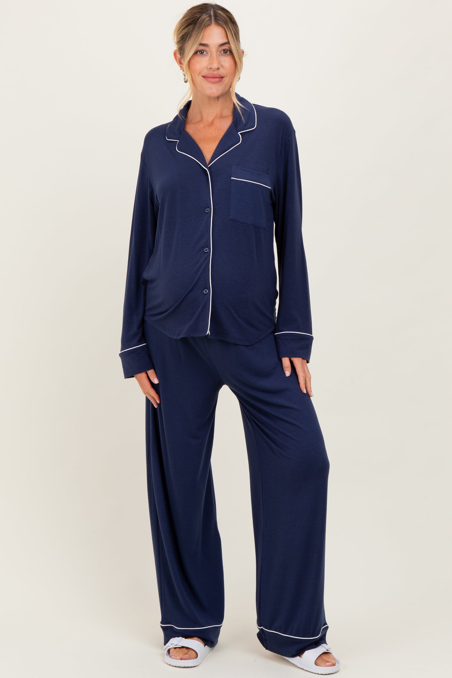 woman wearing a navy blue long sleeve maternity pajama set with white piping details and loose-fitting trousers