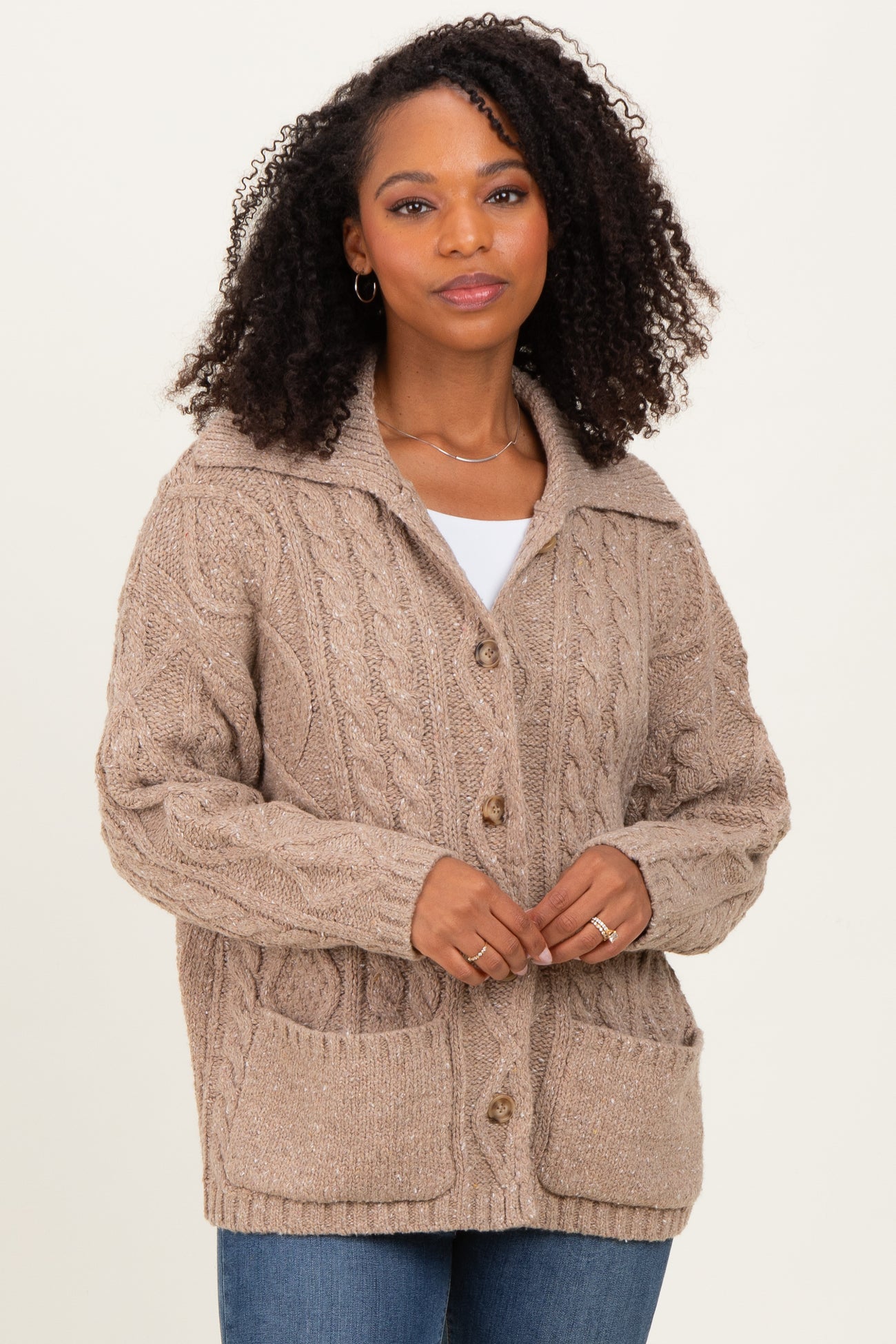 woman wearing a beige cable knit cardigan with a collar and pockets, paired with a white top and blue jeans