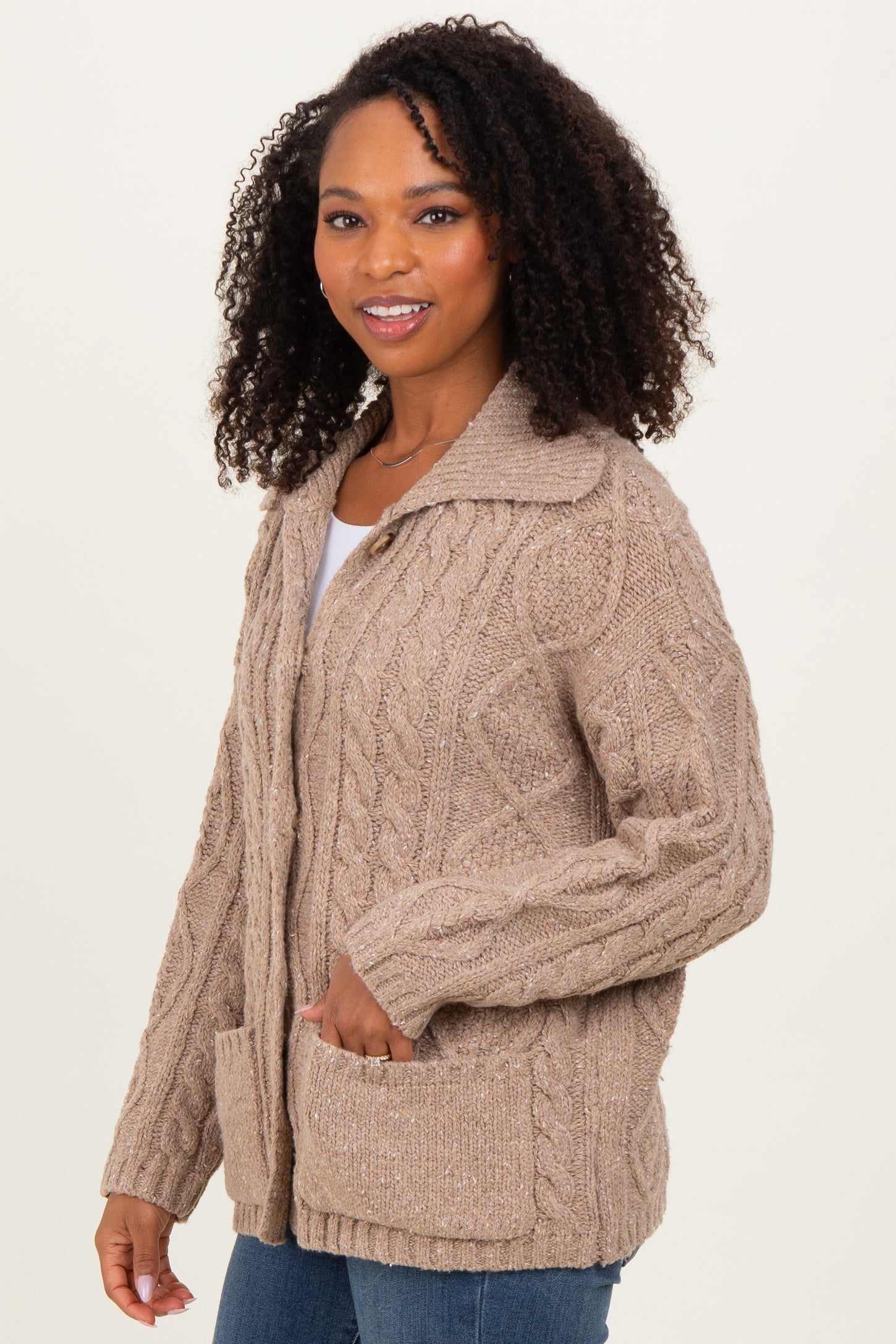 woman wearing a light brown cable knit cardigan with a collar and front pockets, smiling at the camera