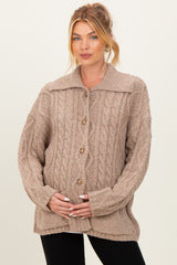 woman wearing a beige cable knit maternity cardigan and holding her baby bump