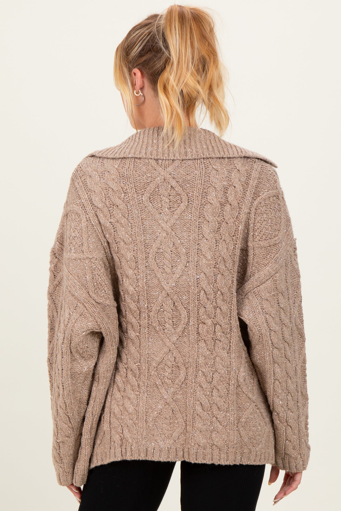 woman wearing a beige oversized cable knit maternity sweater viewed from the back