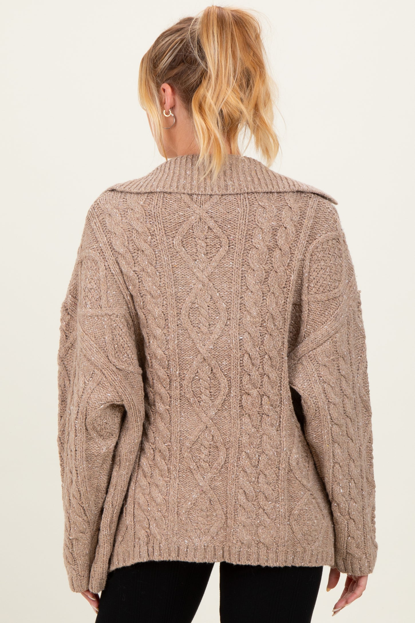 woman wearing a beige oversized cable knit maternity sweater viewed from the back