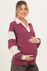 woman wearing a burgundy and cream striped maternity pullover with a collar and holding her baby bump
