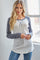 woman wearing a gray and white long sleeve henley top with a lace-up detail and blue jeans