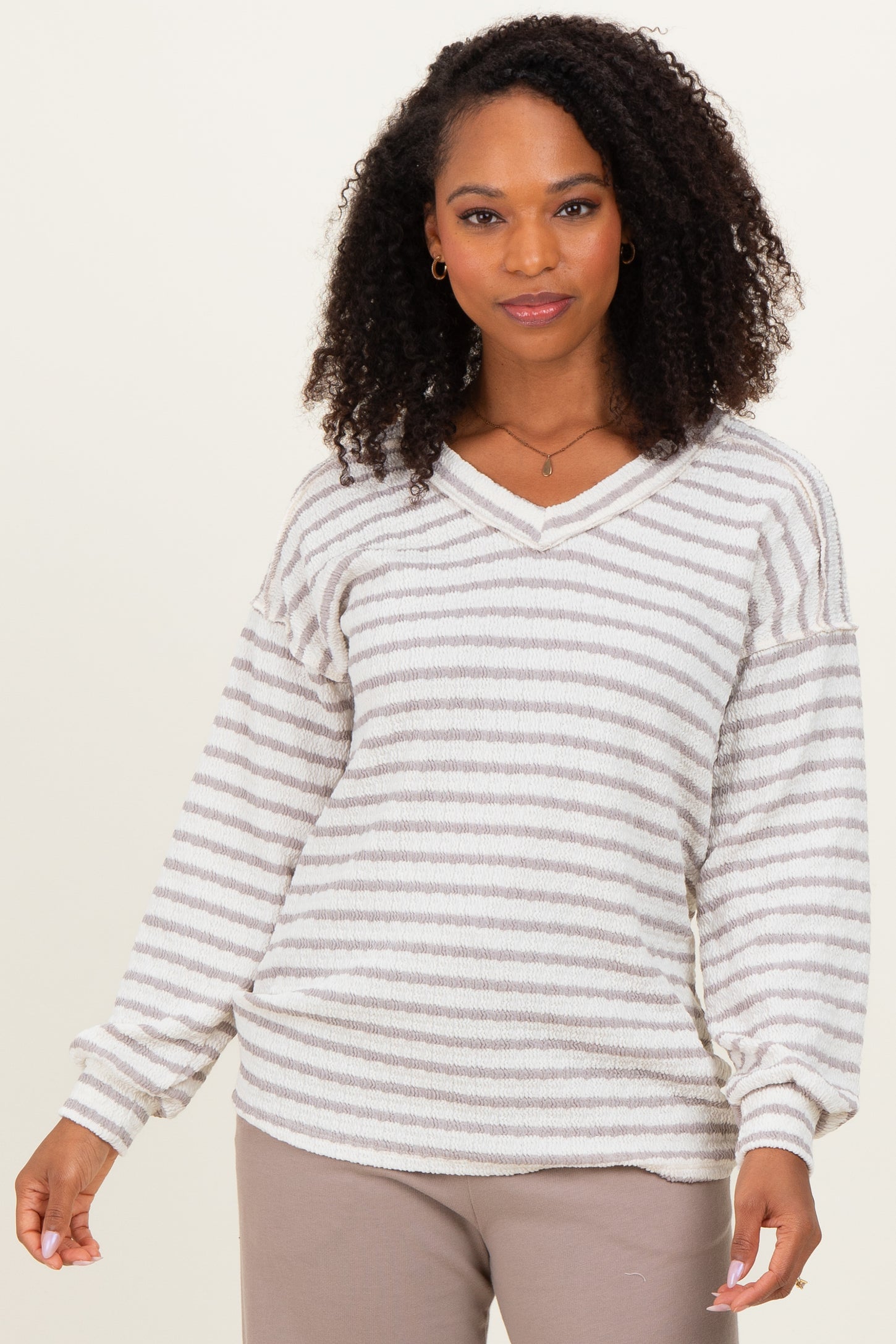 woman wearing a cream and gray striped oversized sweater with a v-neck and balloon sleeves