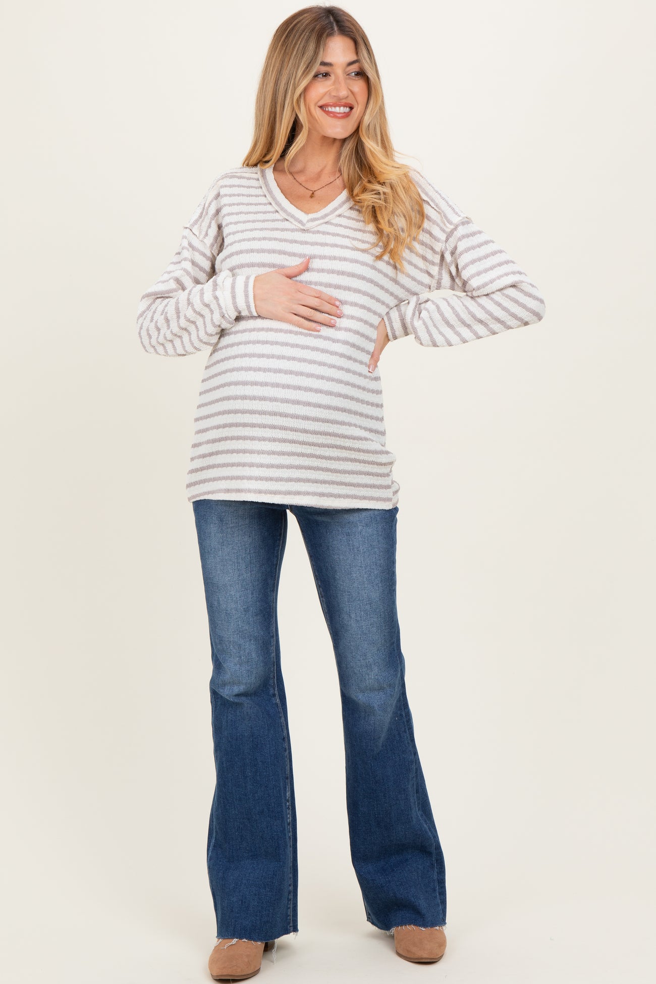 woman wearing a striped maternity sweater with a v-neck and holding her baby bump, paired with flared jeans