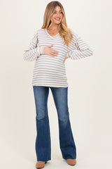 woman wearing a striped maternity sweater with a v-neck and holding her baby bump, paired with flared jeans