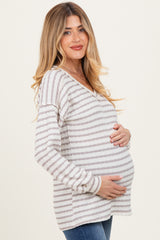 woman wearing a striped maternity sweater in light gray and white, cradling her baby bump