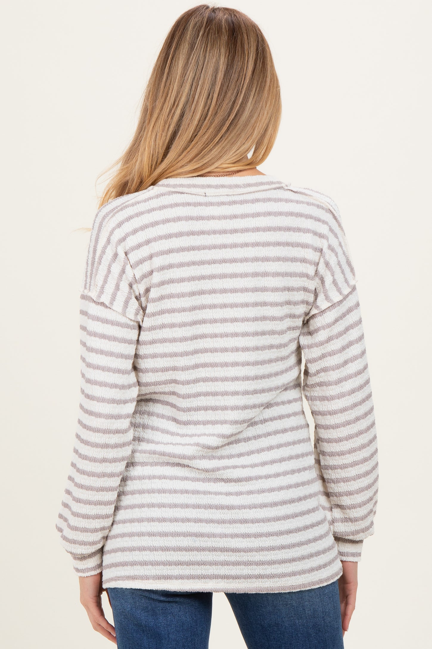 woman wearing a striped cream and gray maternity sweater, shown from the back, styled with relaxed jeans