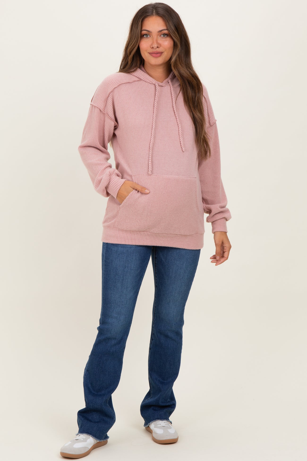 woman wearing a light pink ribbed maternity hoodie with a front pocket and blue flared jeans
