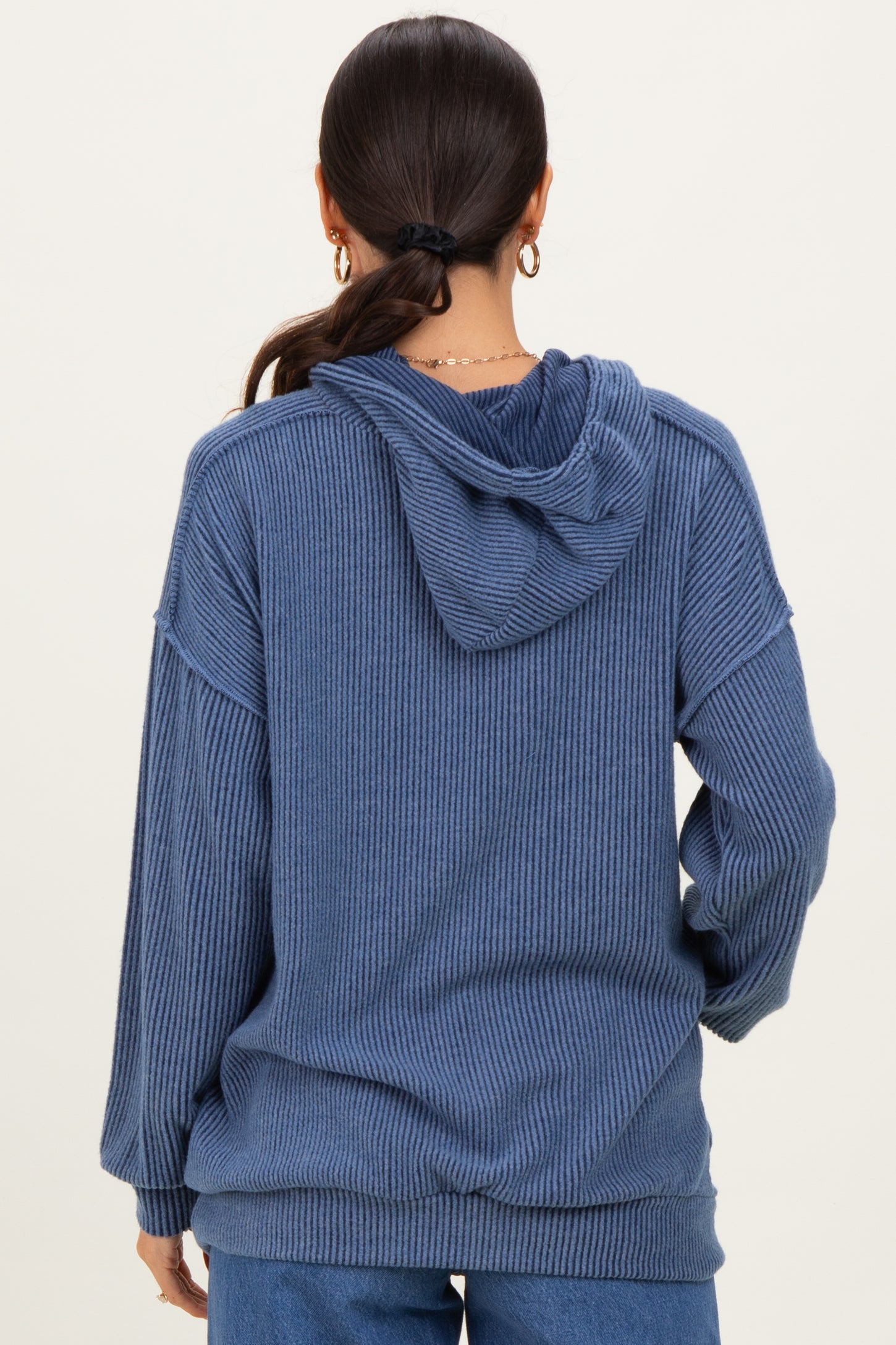 woman wearing a slouchy blue hooded sweater with ribbed texture and a relaxed fit, shown from the back