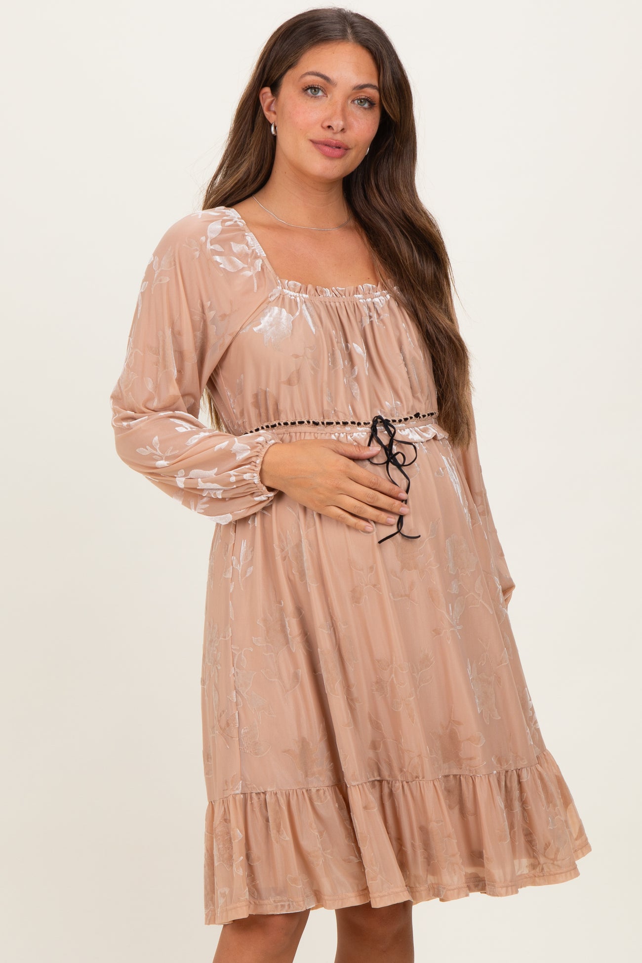 woman wearing a blush maternity dress with long sleeves, floral design, and a drawstring waist, showing her baby bump