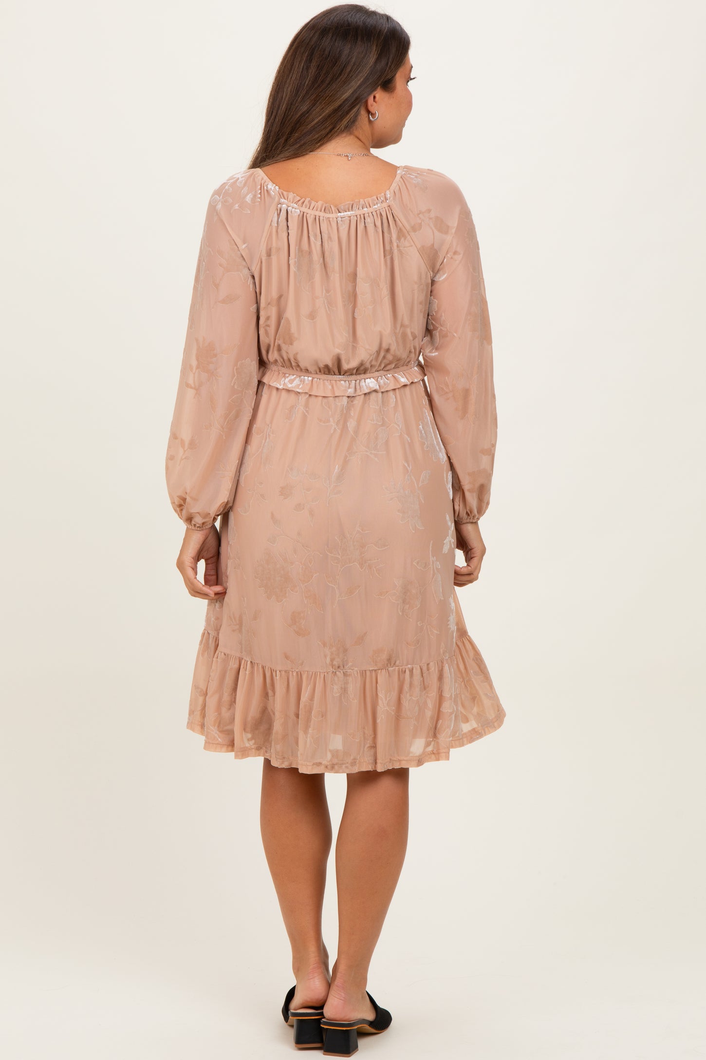 woman wearing a light pink floral maternity dress with long sleeves and a ruffled hem, showing her baby bump from the back
