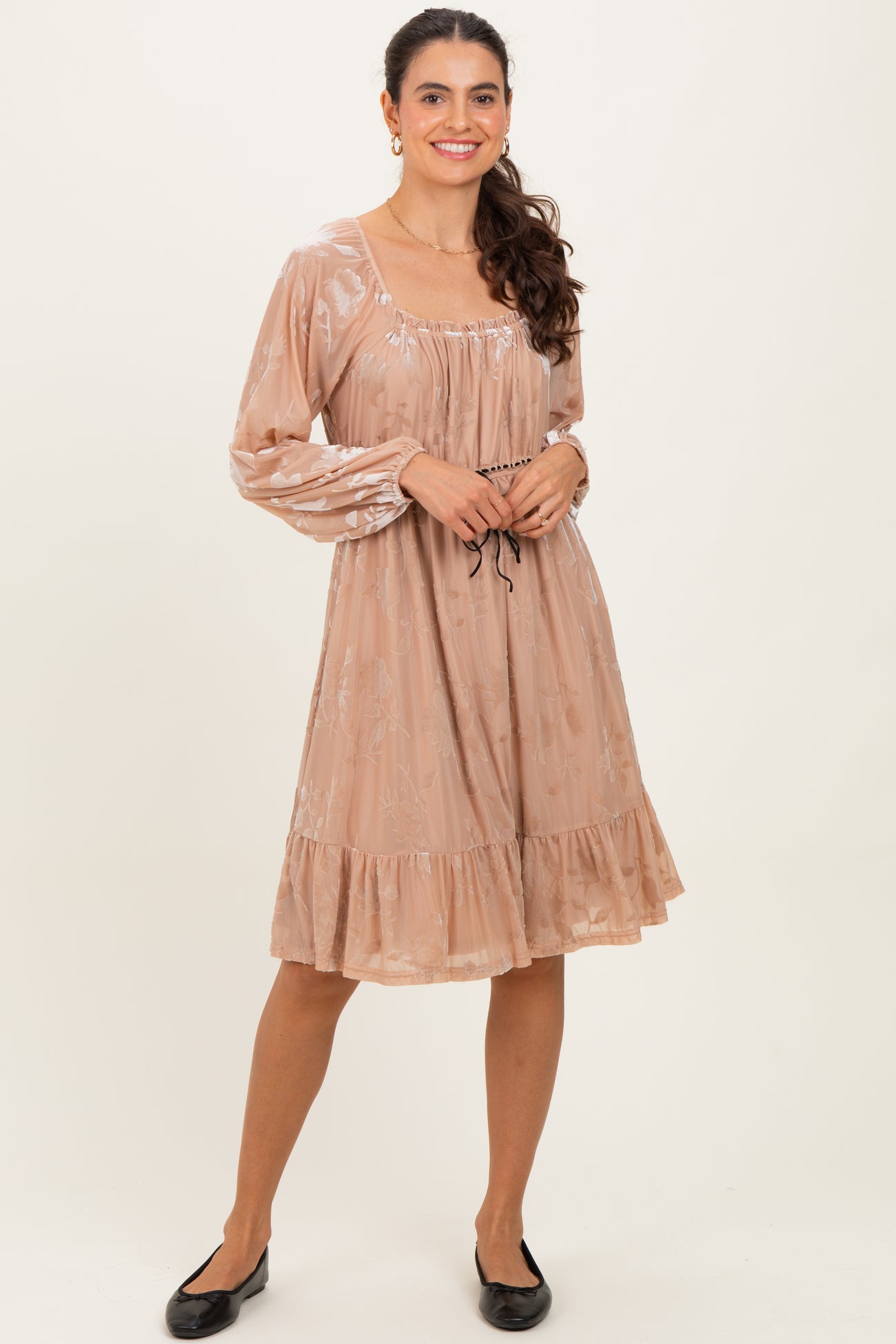 woman wearing a blush pink long sleeve dress with floral print and tiered ruffle hem, styled with flat black shoes