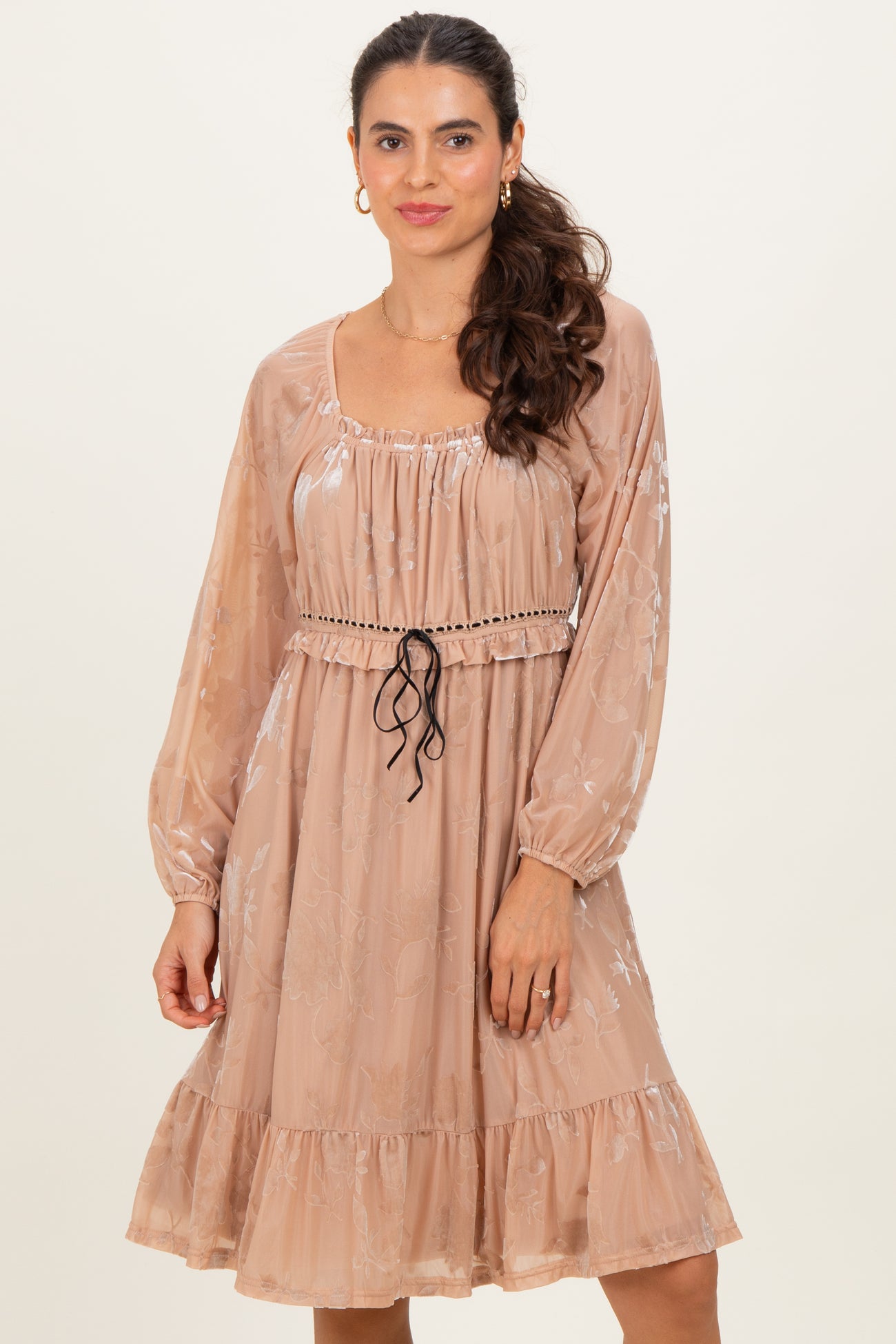 woman wearing a beige floral patterned long sleeve dress with a cinched waist and ruffled hemline