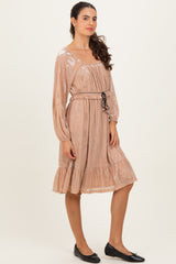 woman wearing a beige long sleeve dress with a ruffled hem and adjustable drawstring waist, styled with black flats