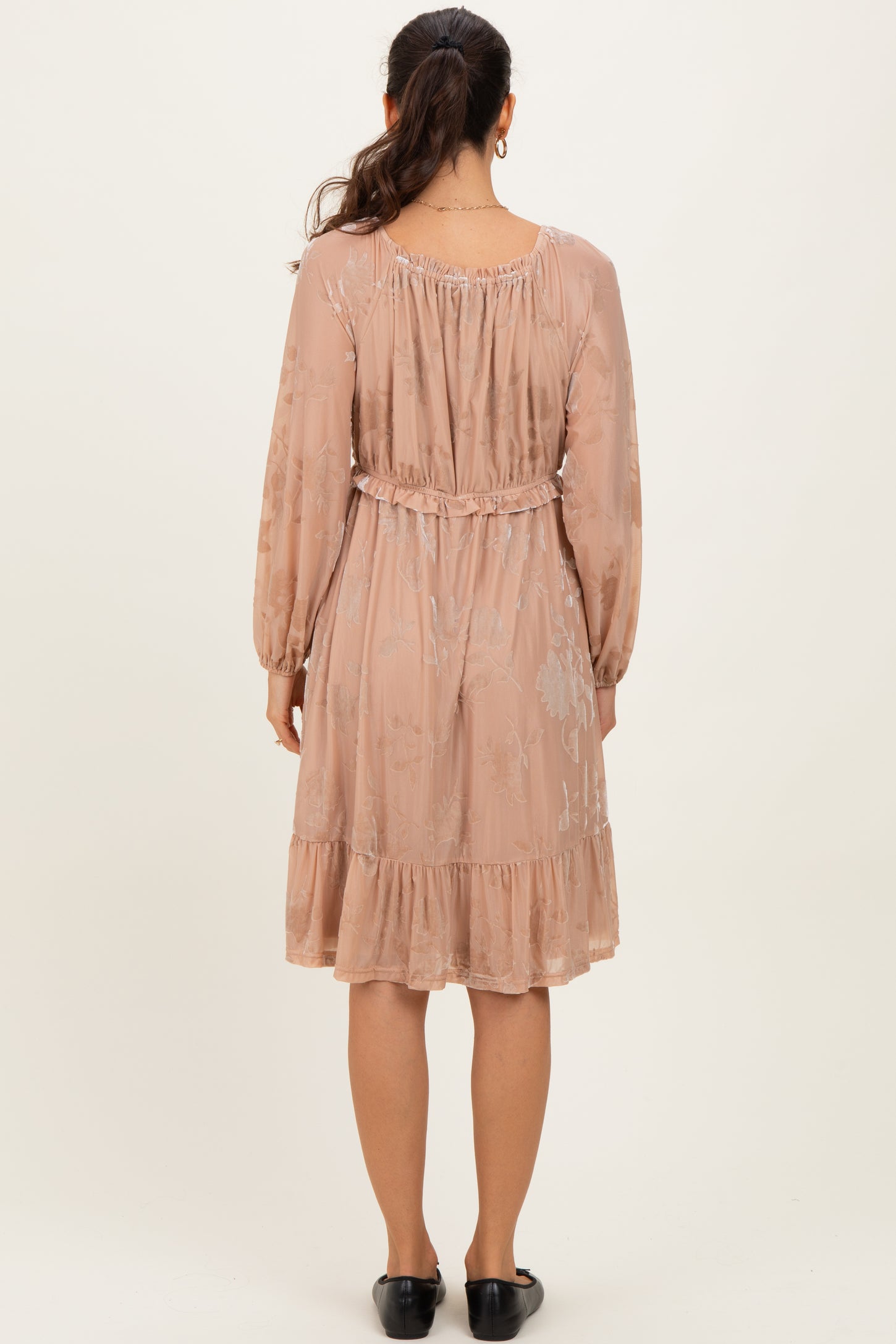 woman wearing a blush pink long sleeve dress with a cinched waist and ruffled hem, seen from the back