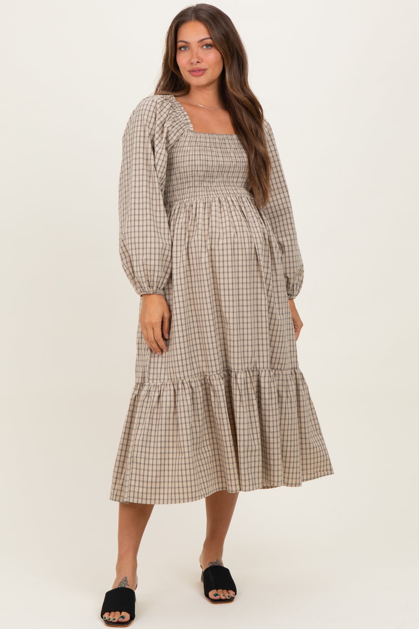 woman wearing a beige checkered maternity dress with long sleeves and a tiered frill hem, baby bump visible