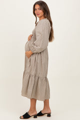 woman wearing a beige and white checkered maternity dress with long sleeves and ruffle hem, holding her baby bump