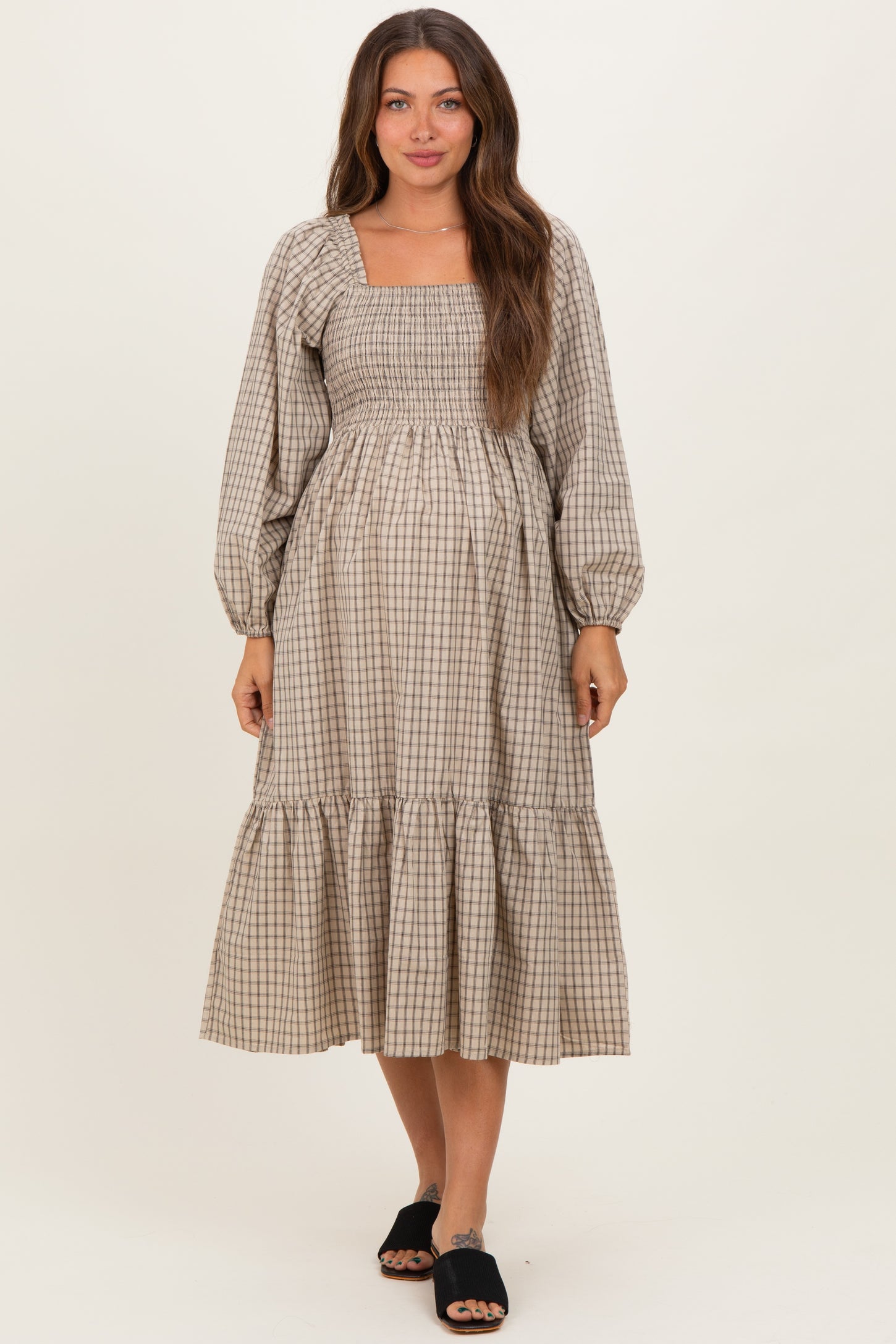 woman wearing a beige checkered maternity dress with puff sleeves and a tiered skirt, showcasing her baby bump