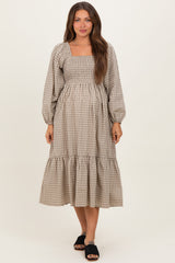 woman wearing a beige checkered maternity dress with puff sleeves and a tiered skirt, showcasing her baby bump