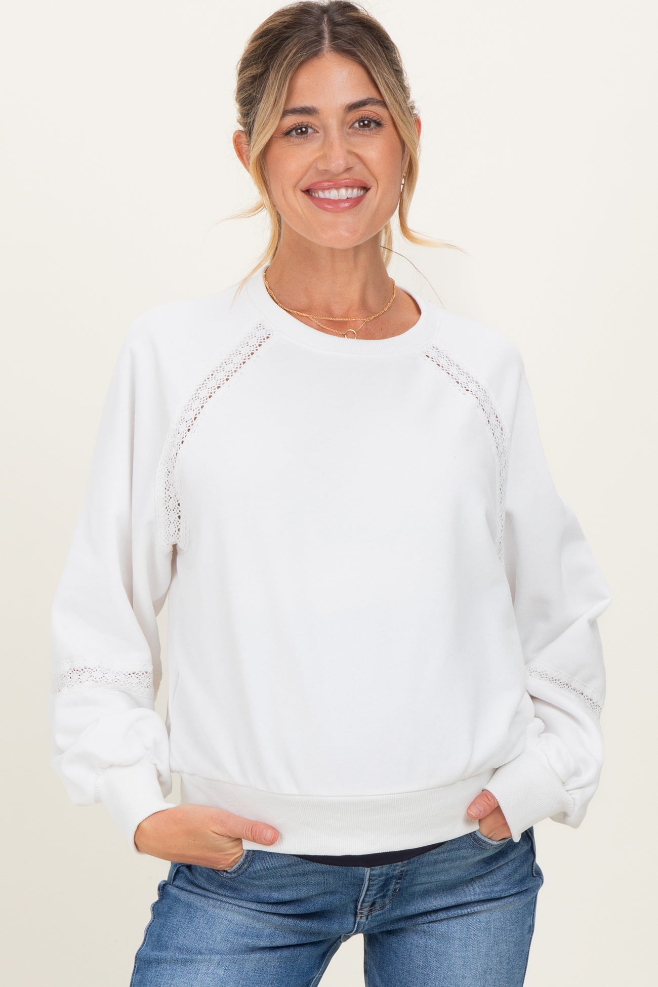 woman wearing a white maternity sweatshirt with lace details and relaxed fit, smiling with hands in pockets