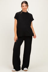 woman wearing a black ribbed maternity top and matching wide-leg pants, showing a visible baby bump