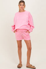 woman wearing a pink maternity sweatshirt and matching shorts, standing with hands in pockets
