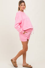 woman wearing a pink maternity sweatshirt and matching shorts with pockets, featuring a drawstring waist