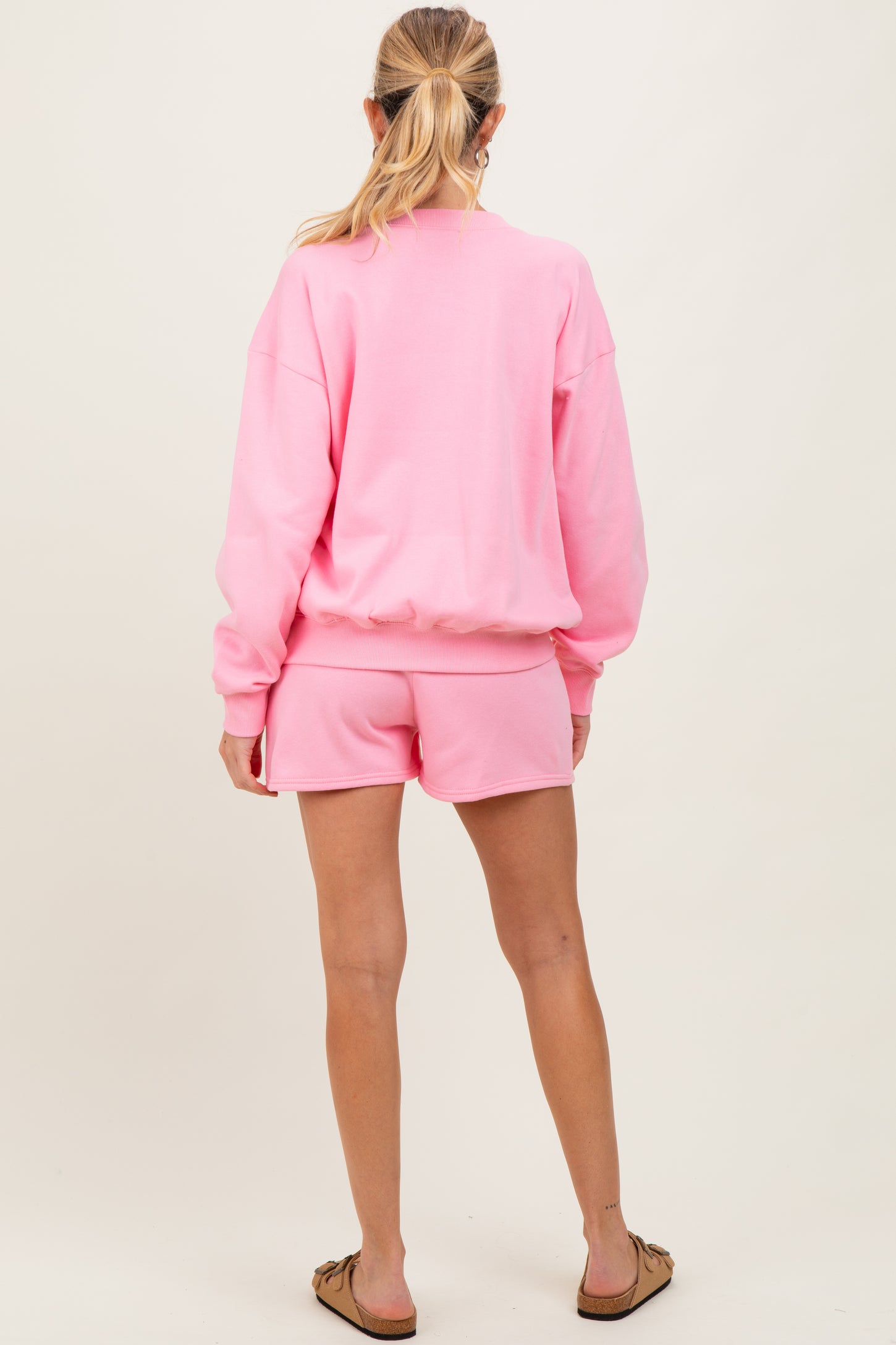 woman wearing a pink maternity sweatshirt and matching shorts, viewed from the back