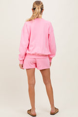 woman wearing a pink maternity sweatshirt and matching shorts, viewed from the back
